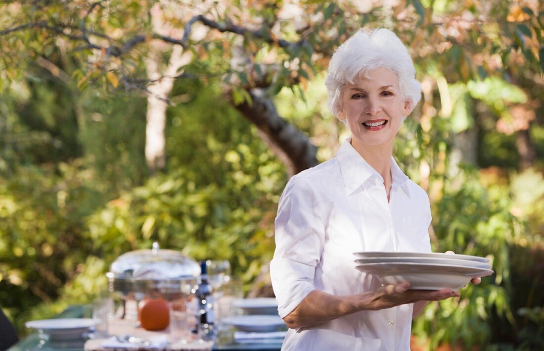 Senior woman standing in garden holding stack of plates