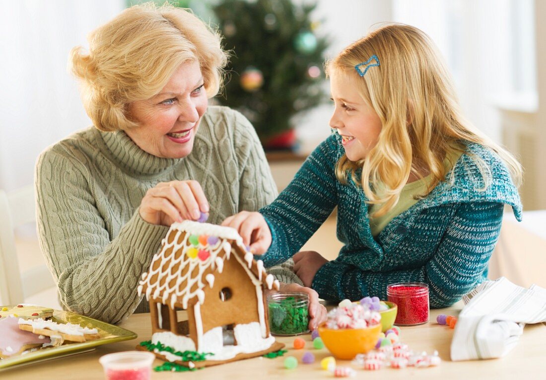 Grandmother with granddaughter (8--9) making gingerbread house