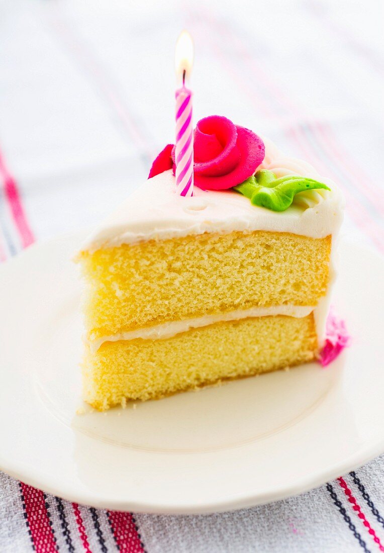 Ein Stück Kuchen mit Zuckerrose und Kerze