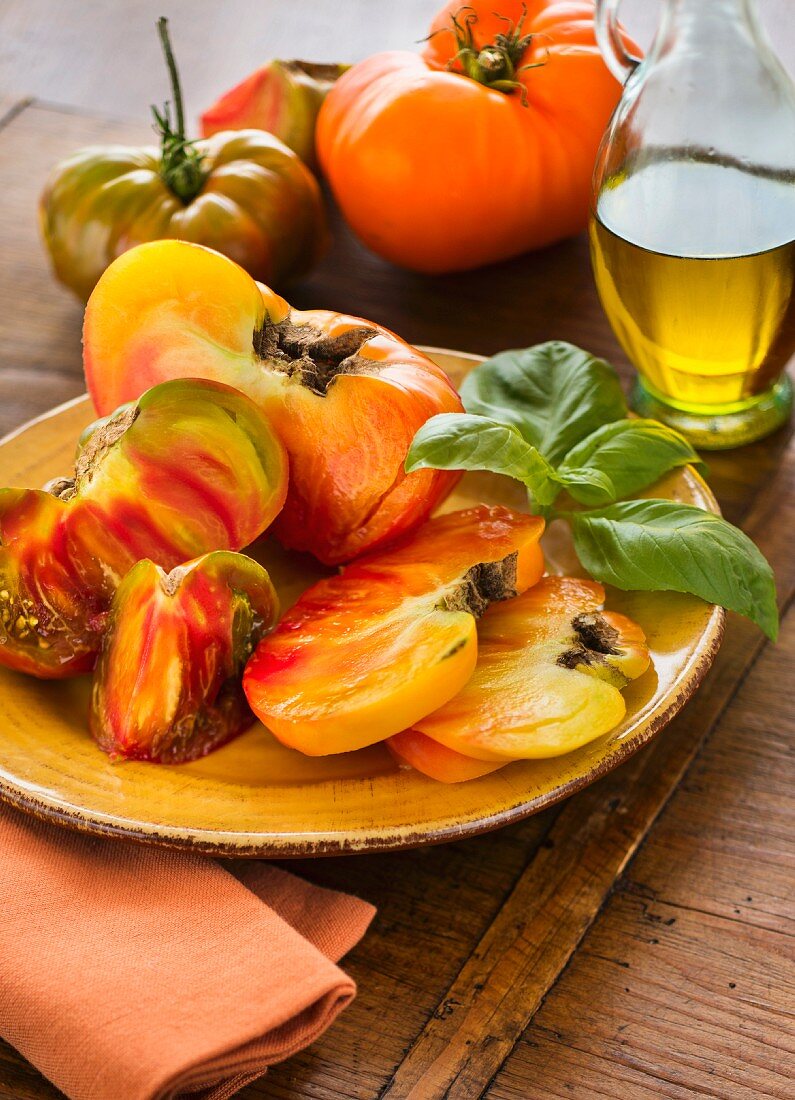 Aufgeschnittene Heirloom Tomaten mit Basilikum auf einem Teller und Olivenöl