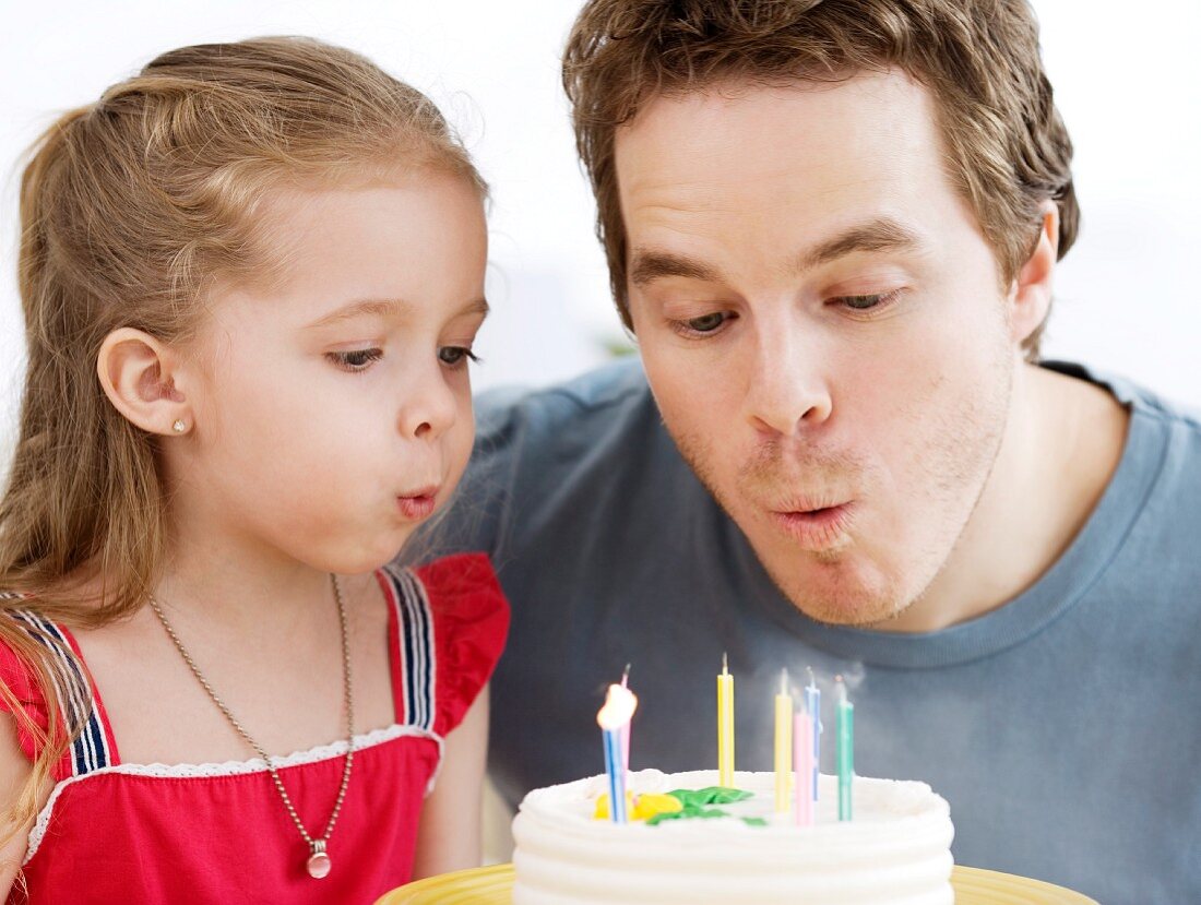 Vater und Tochter blasen die Geburtstagskerzen aus