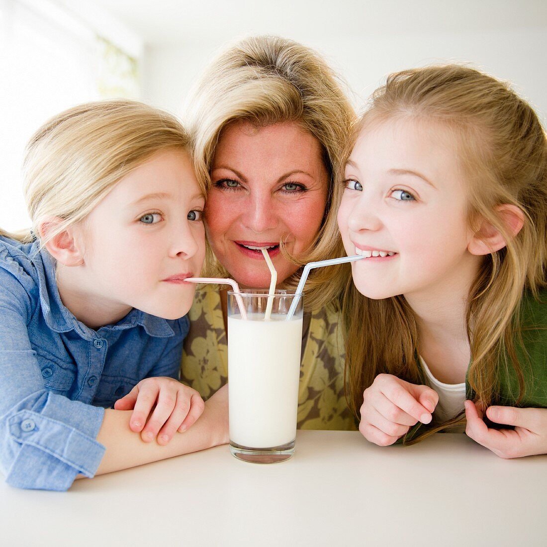 Mutter mit zwei Töchtern trinken mit Strohhalmen aus einem Glas Milch