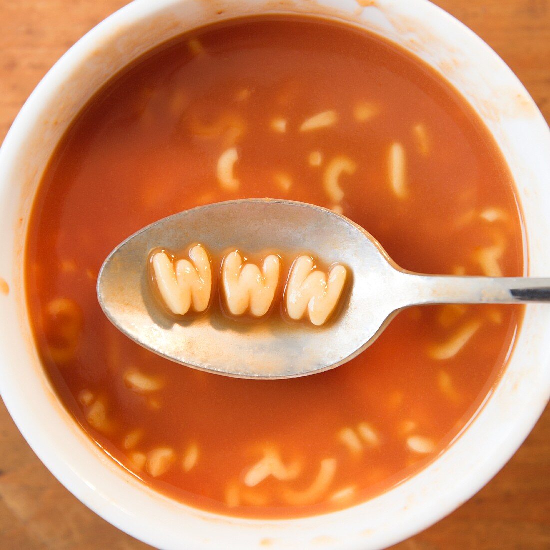 Close up of soup with letter noodles on spoon forming www site