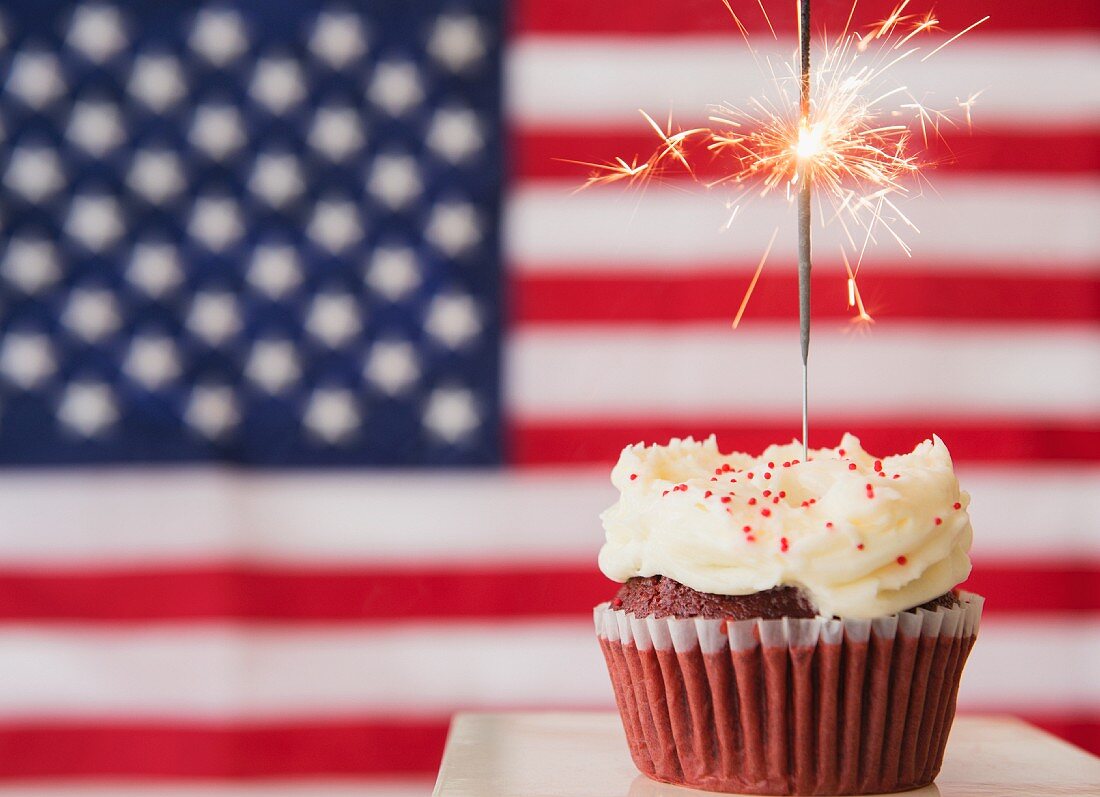 Studio shot of sparkler atop cupcake, american flag in background