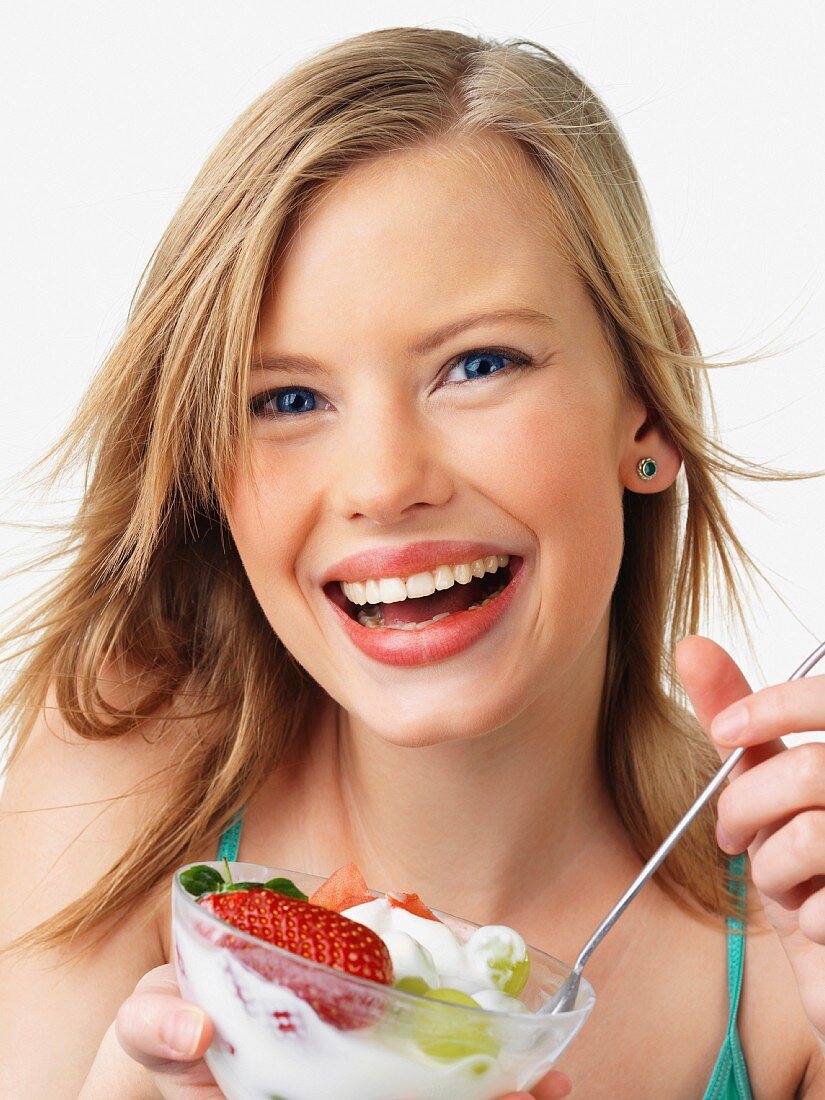 Strahlende junge Frau isst einen Fruchtsalat mit Joghurt