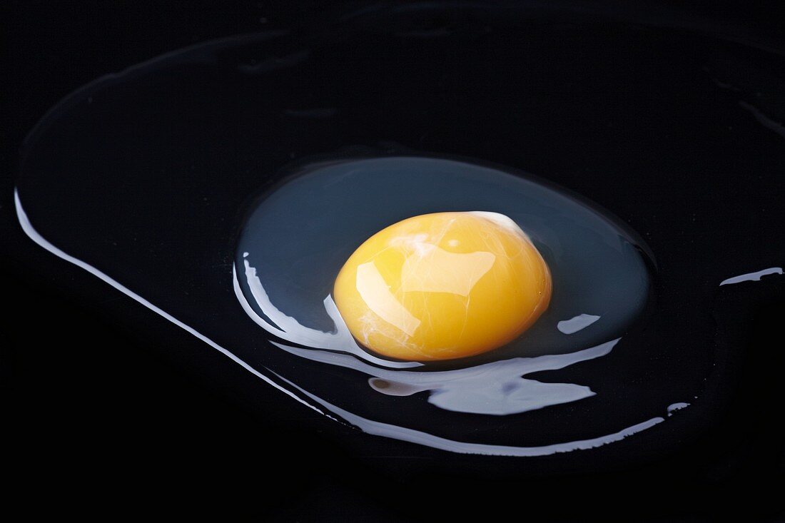 Raw egg out of its shell, against a black background