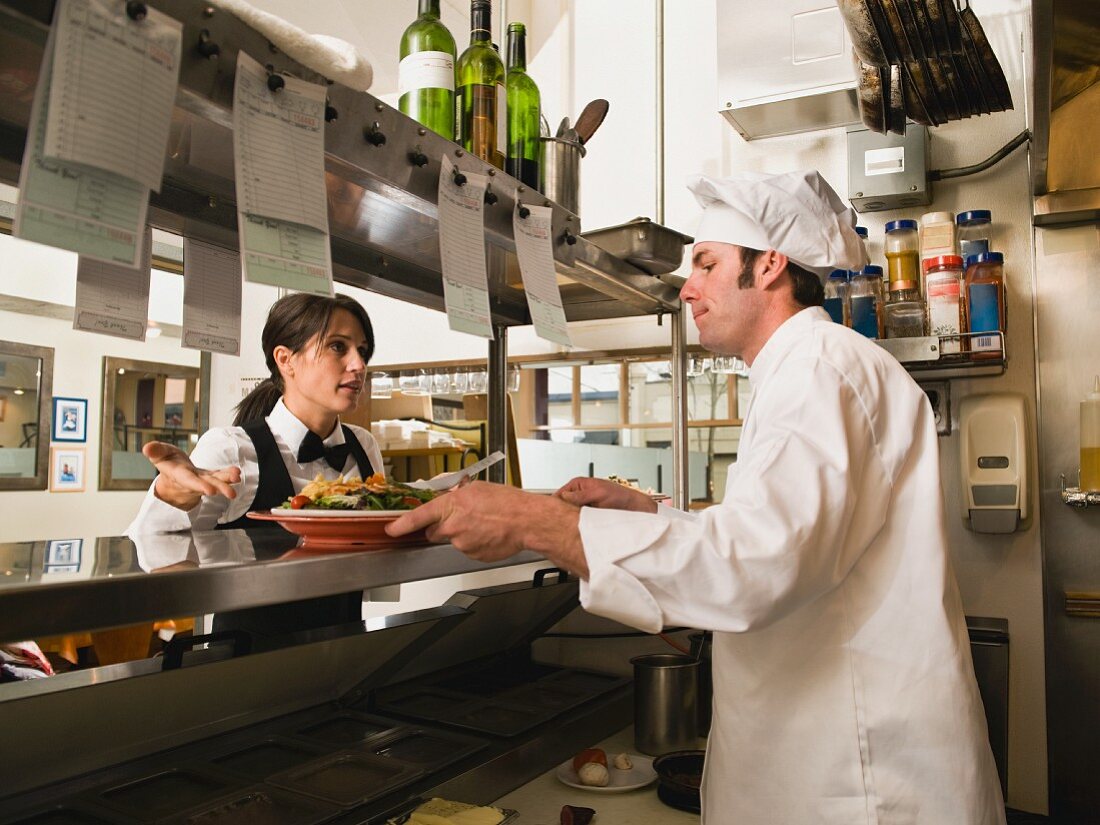 Waitress gesturing to chef in restaurant kitchen