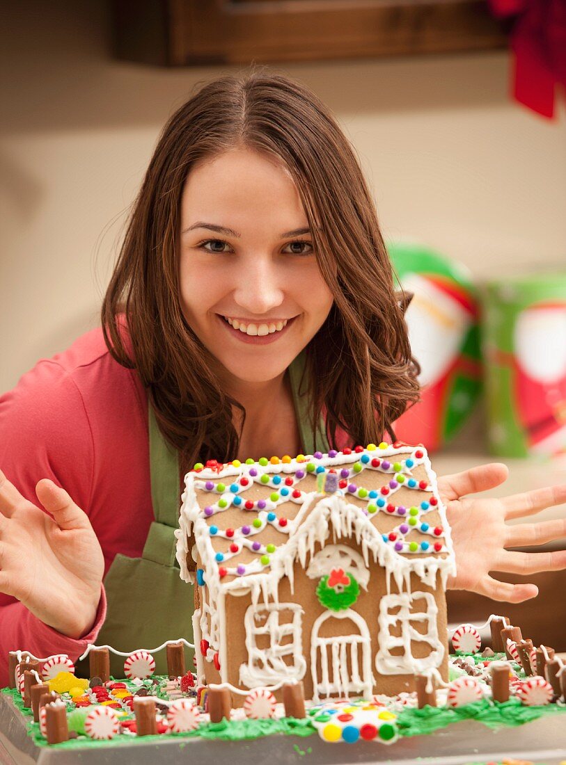 Portrait of young woman with gingerbread house in kitchen