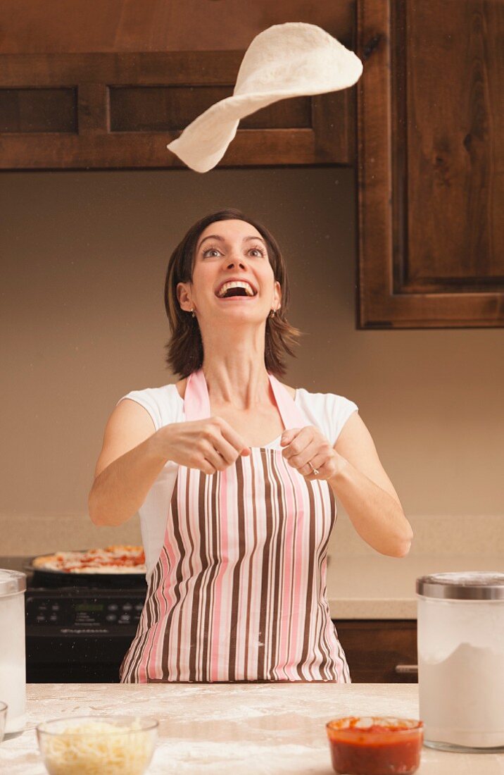 Woman tossing dough in kitchen
