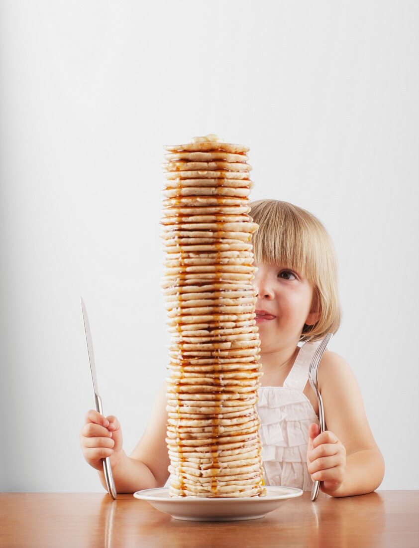Mädchen sitzt hinter einem hohen Stapel Pfannkuchen