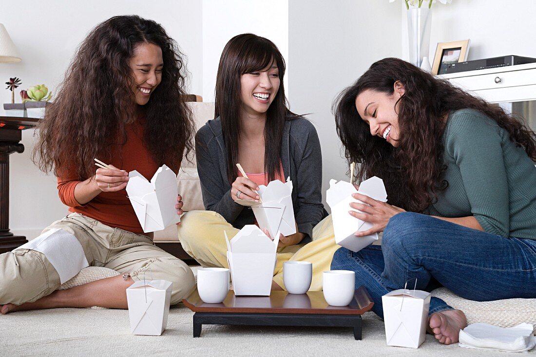 Three female friends eating take out food at home