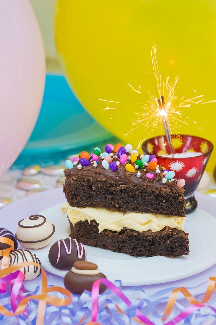 Ein Stück Schokoladenkuchen mit bunten Süssigkeiten für eine Party, Wunderkerze, Konfekt