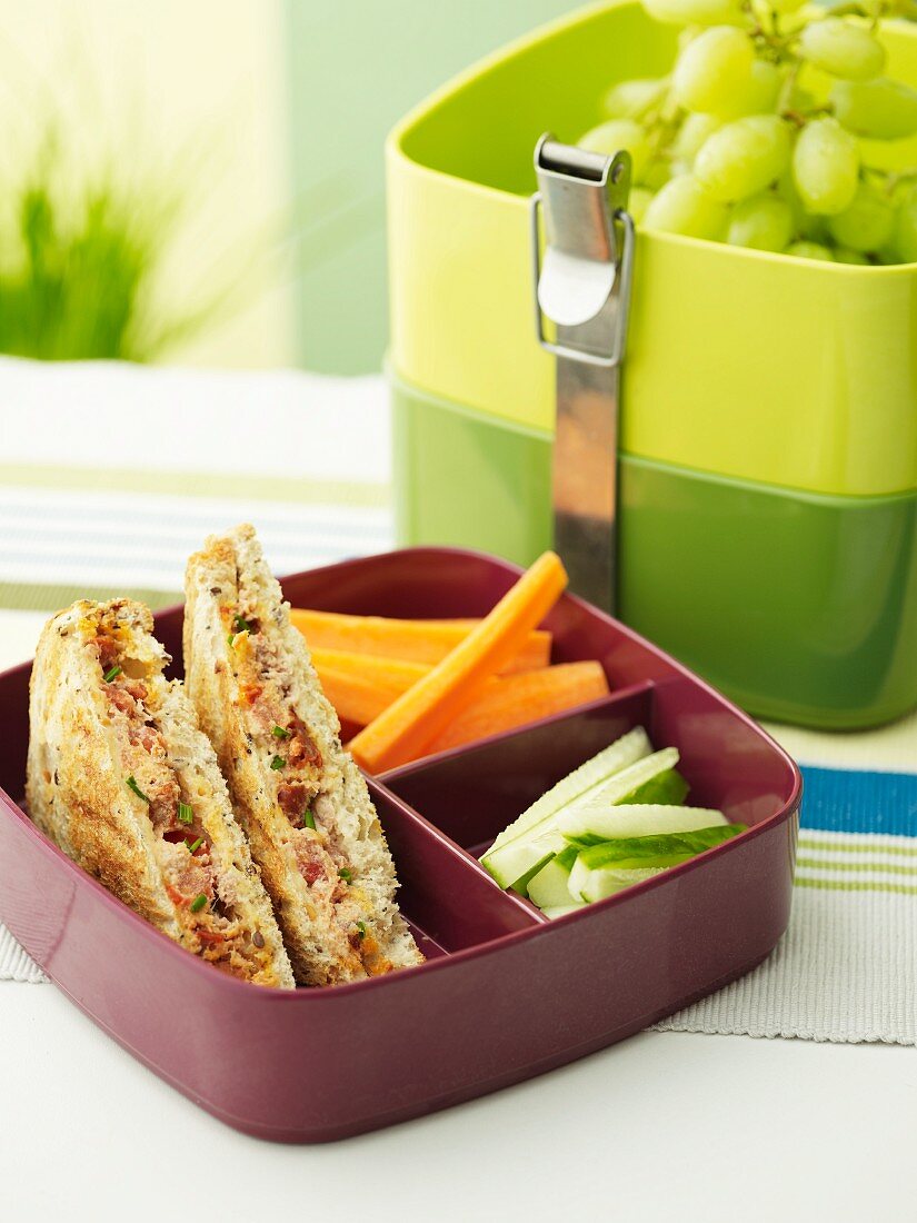 Sandwiches with tuna fish, tomatoes and chorizo, vegetables and grapes in a lunch box