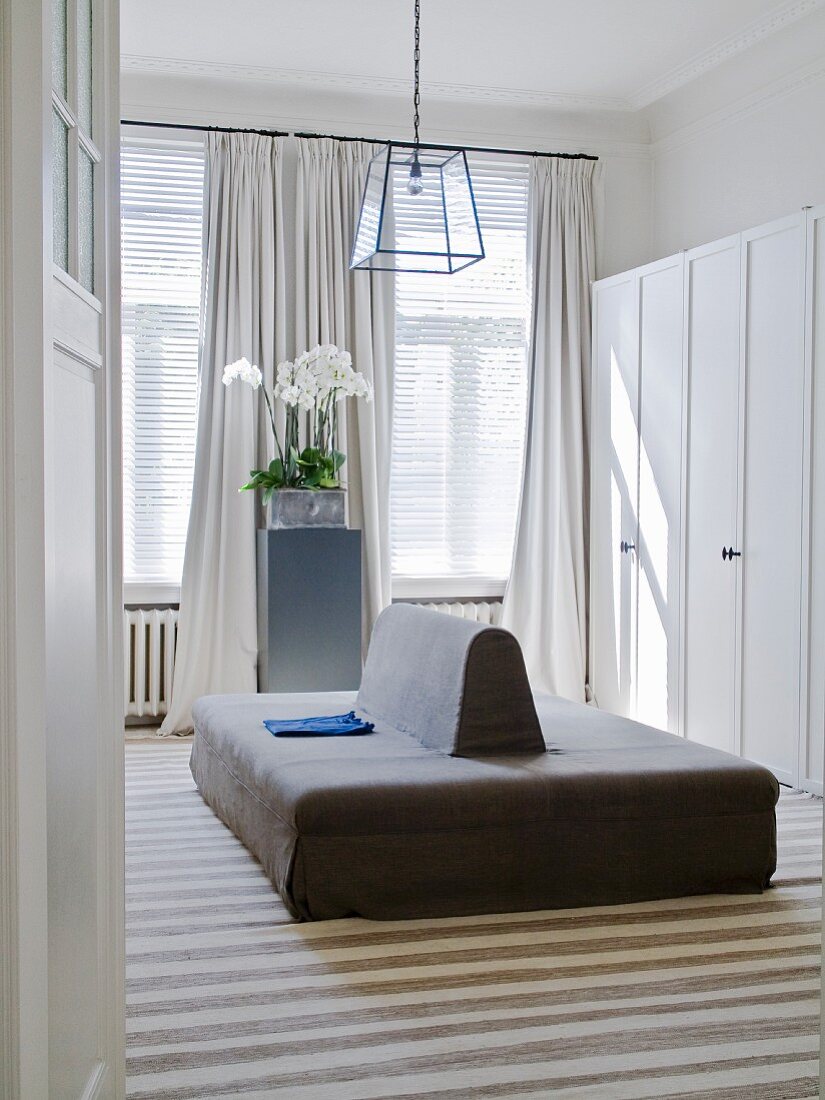 View through open door of double-sided sofa in front of white wardrobes in dressing room with traditional ambiance