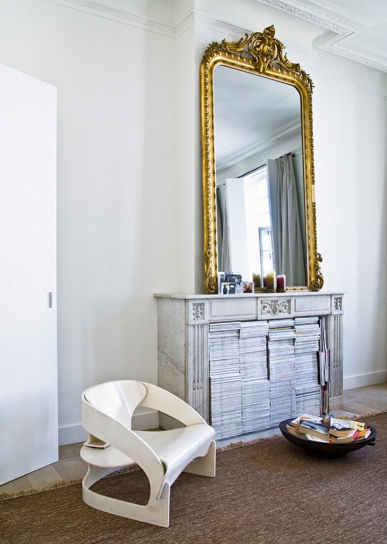 Collection of magazines in disused open fireplace, gilt-framed mirror and modern, retro-style chair