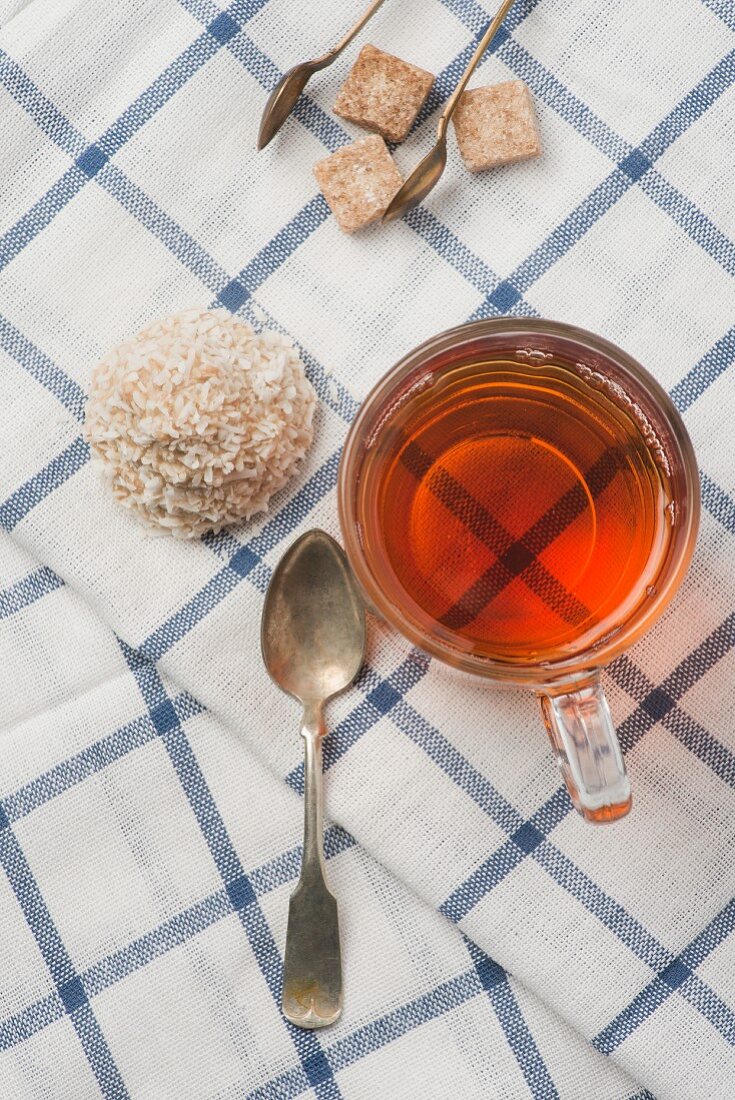 A glass of tea and a coconut macaroon on a checked tea-towel