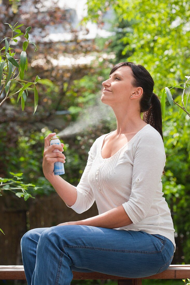 Frau befeuchtet ihr Gesicht mit Wasserspray