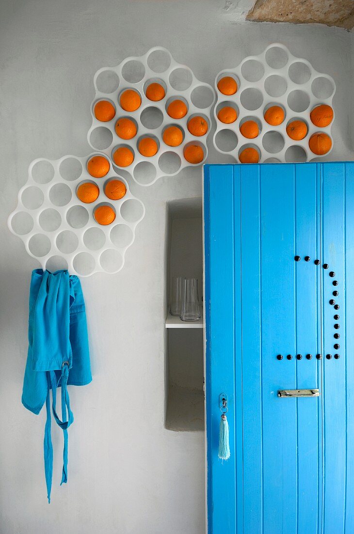 Perforated frames on wall used for decorative orange storage; open door and apron in matching turquoise blue