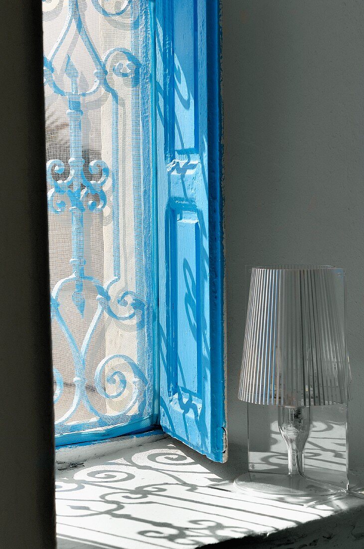 Window recess with blue wooden shutters and pattern of light cast by grille