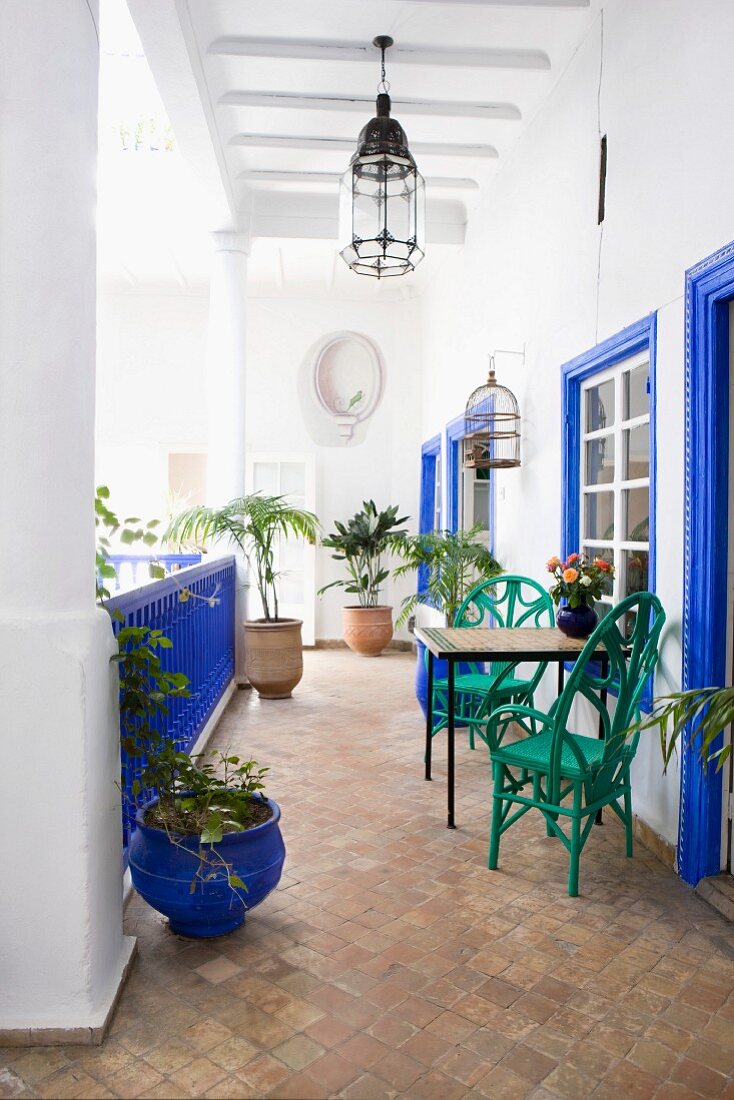 Grüne Stühle vor leuchtend blau lackierten Fensterumrahmungen und Geländer auf der Veranda eines marokkanischen Innenhofs