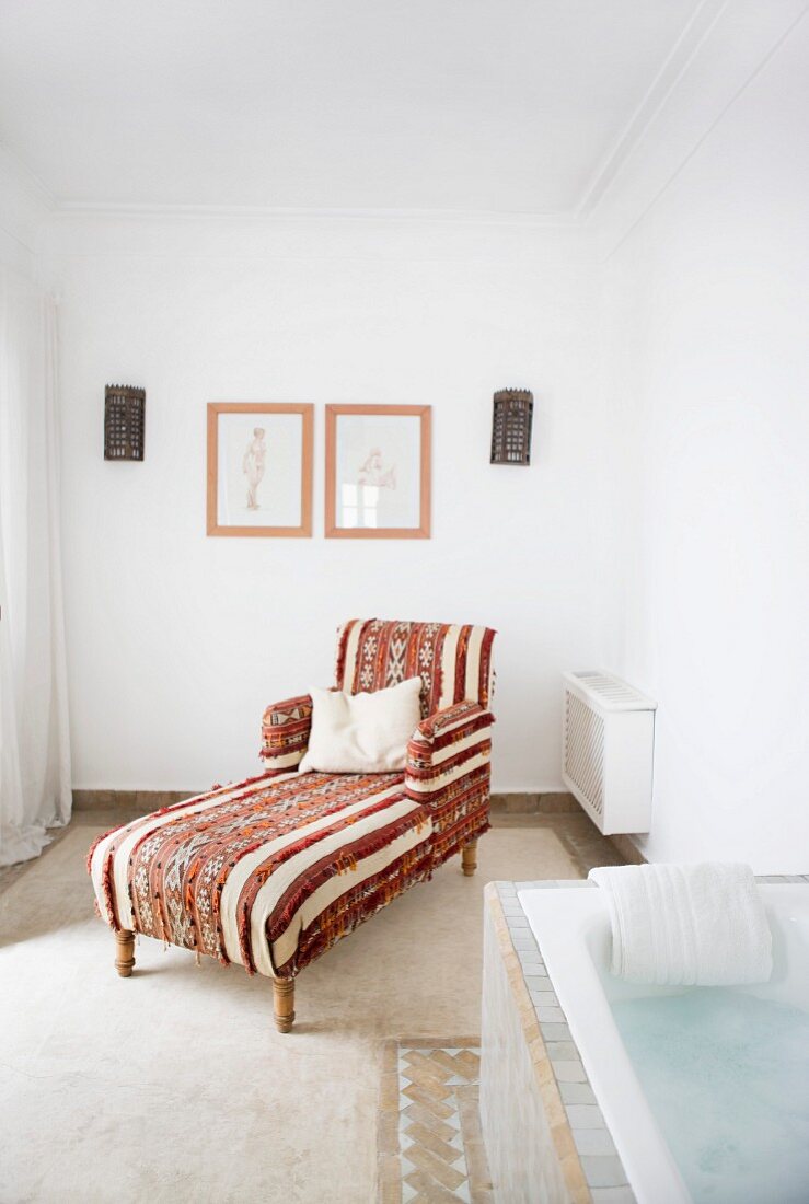 Antique chaise longue with Oriental fabric cover in cosy bathroom with masonry bathtub