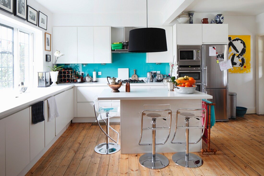 Pendant lamps with black lampshades above modern island counter in open-plan kitchen with barstools on wooden floor