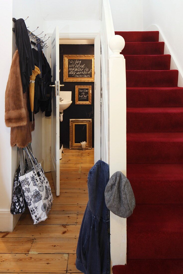 Red carpet on staircase in traditional stairwell with open door showing view of gilt picture frames in bathroom