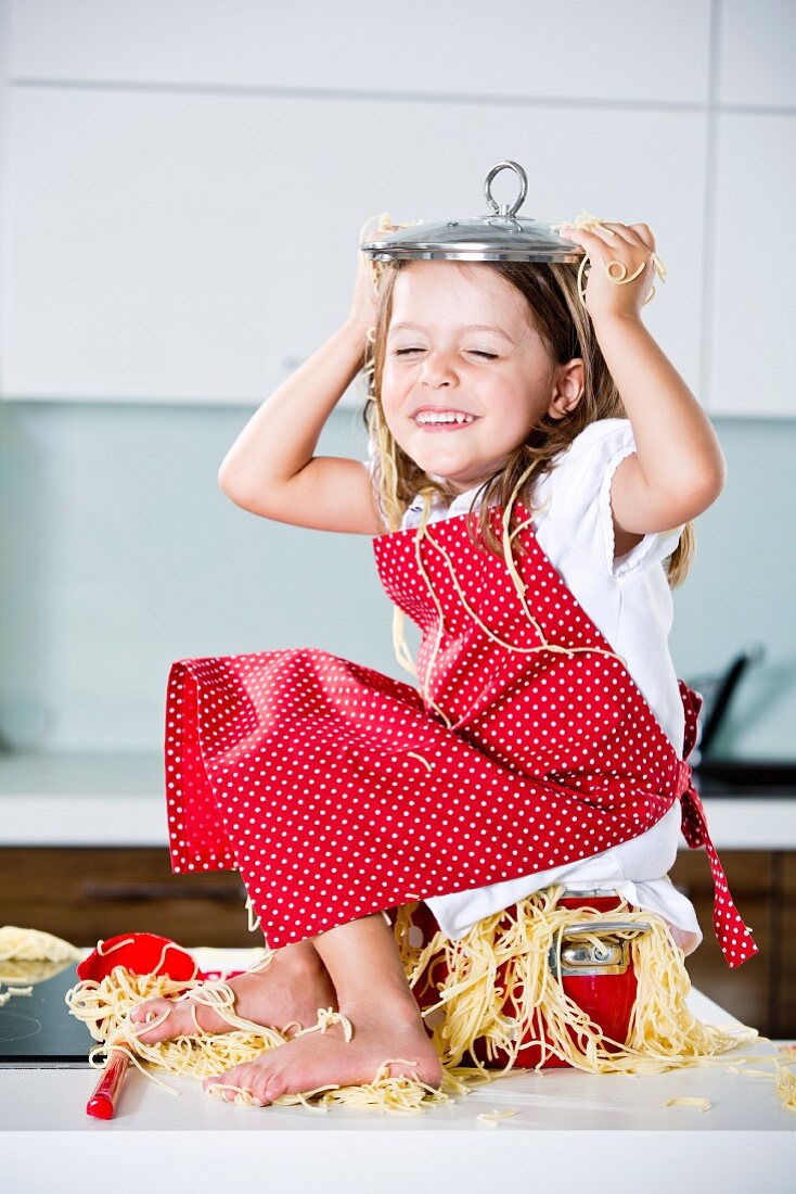Mädchen spielt mit Spaghetti auf Arbeitsplatte in der Küche