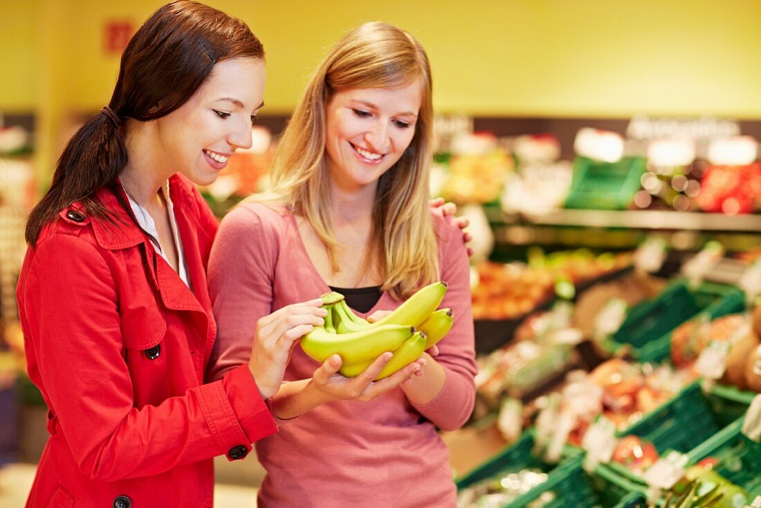 Germany, Cologne, Young women with bananas in supermarket