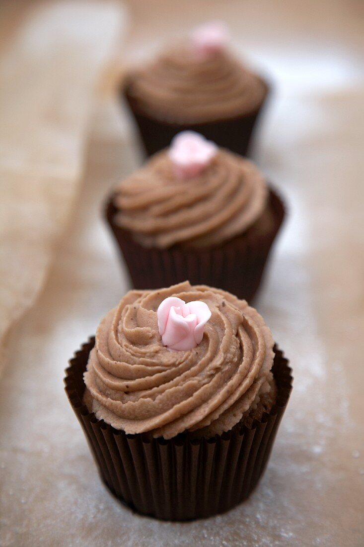 Drei Schokoladen-Cupcakes mit rosa Zuckerblüte