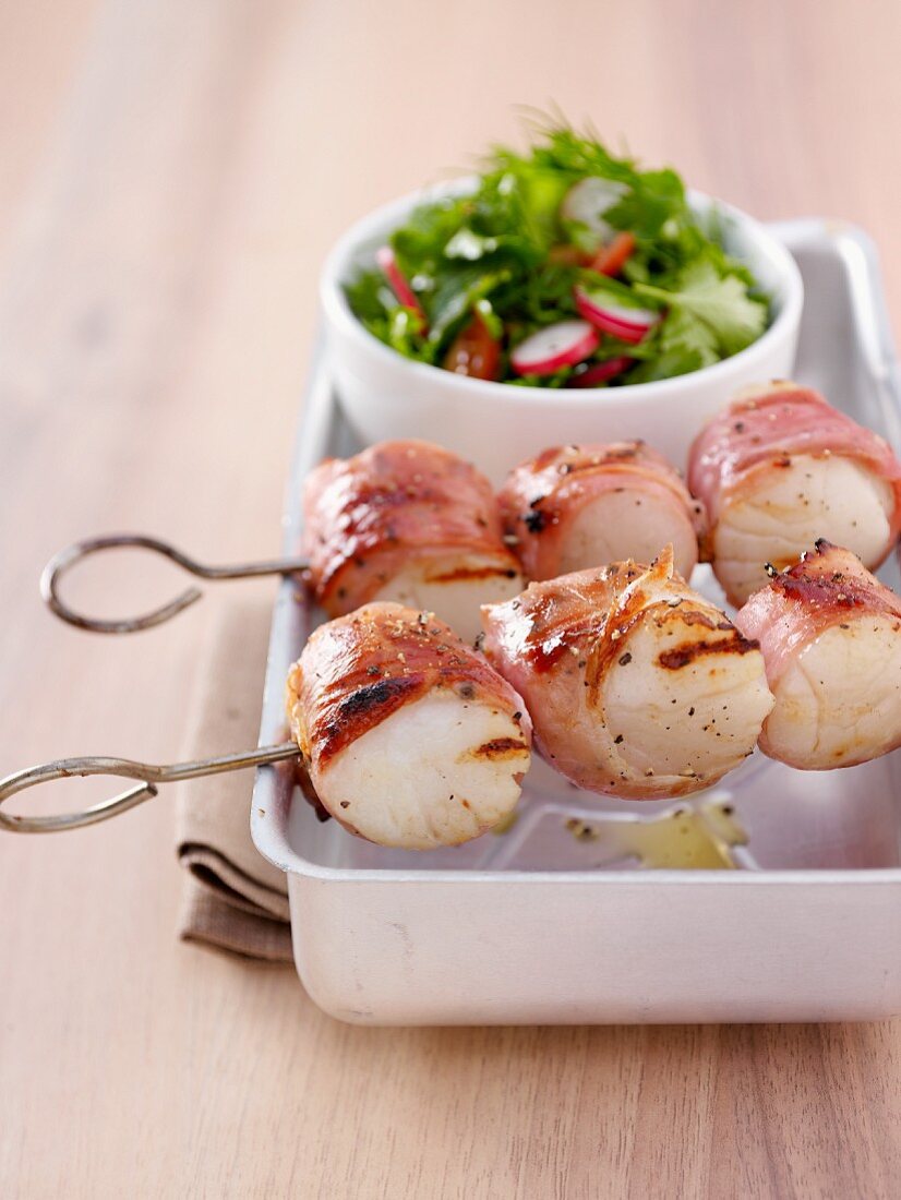 Scallops wrapped in bacon on a skewer and a side of salad