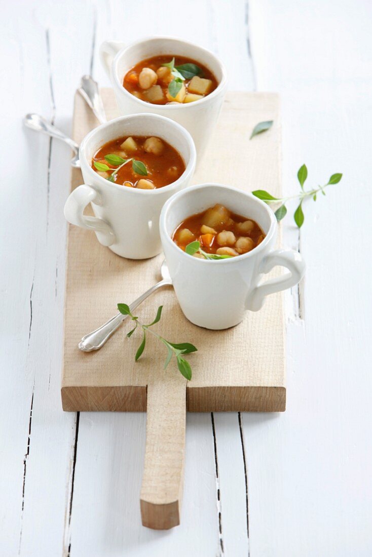 Cups of potato chickpea soup on chopping board