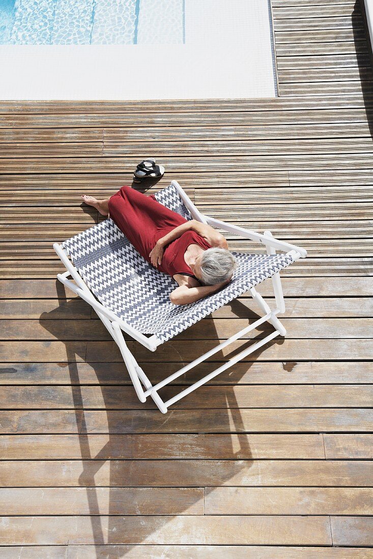 Spain, Senior woman relaxing on deck chair at beach