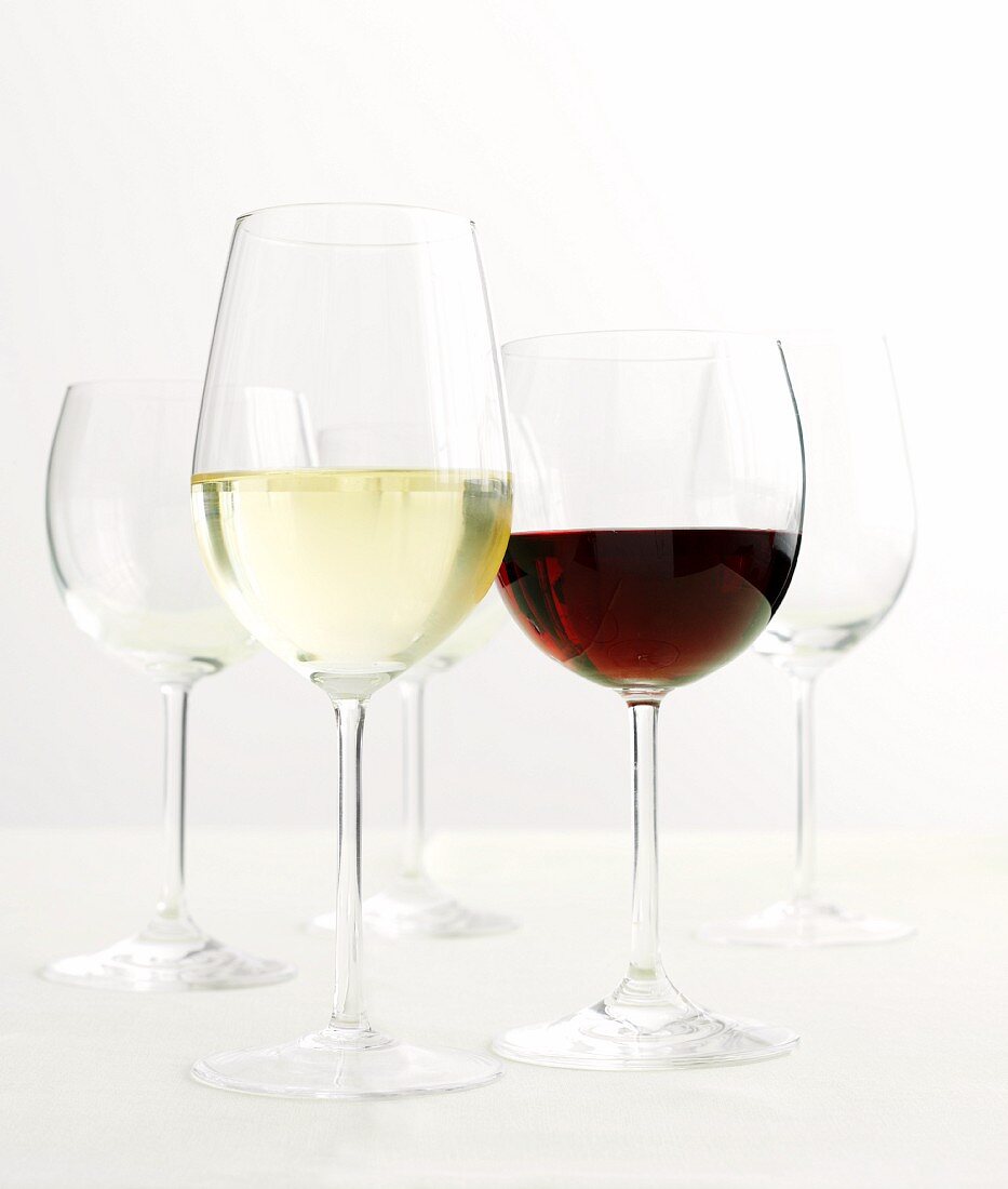 A glass of white wine, a glass of red wine and empty wine glasses