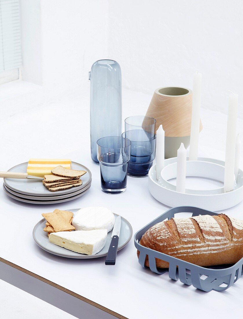 Gedeckter Tisch mit Brot, Käse, Kerzen, Vasen und Gläsern