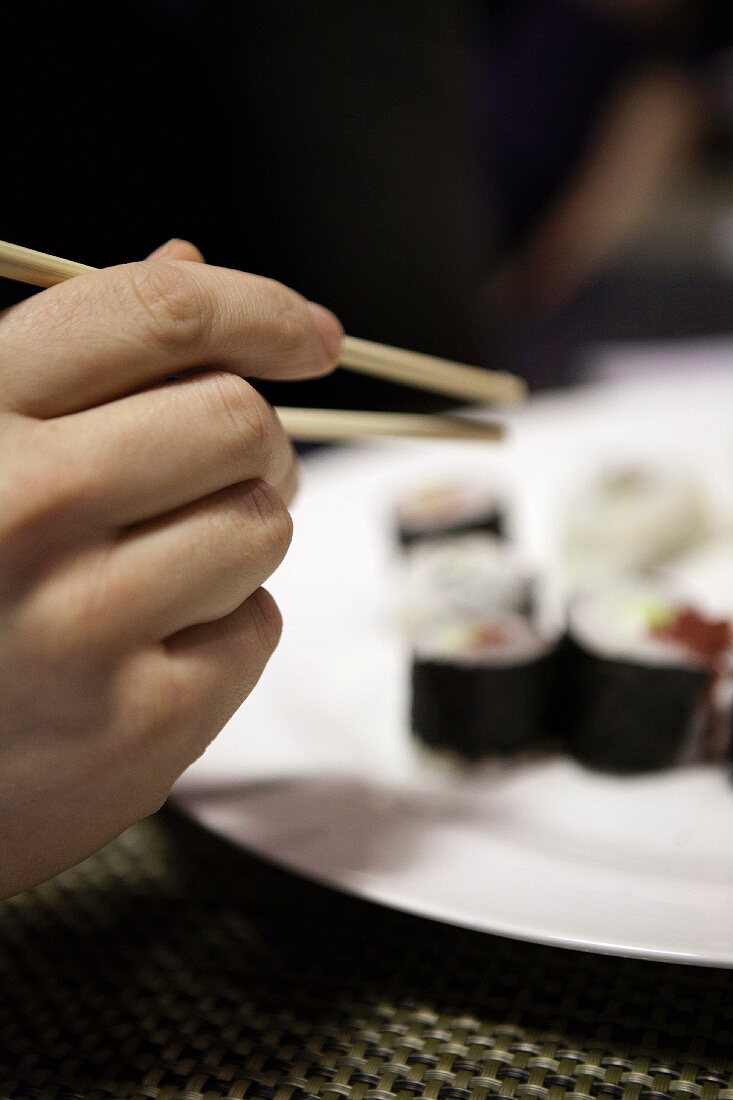 A hand reaching for a piece of sushi using chopsticks