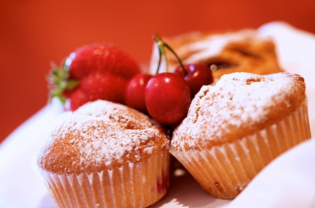 Muffins dusted with icing sugar, with cherries and a strawberry