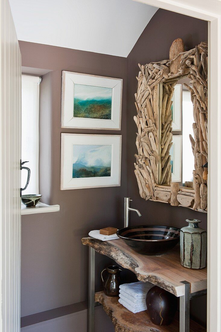 Rustic washstand under bathroom mirror with artistic driftwood frame; two modern watercolour landscapes on wall to one side