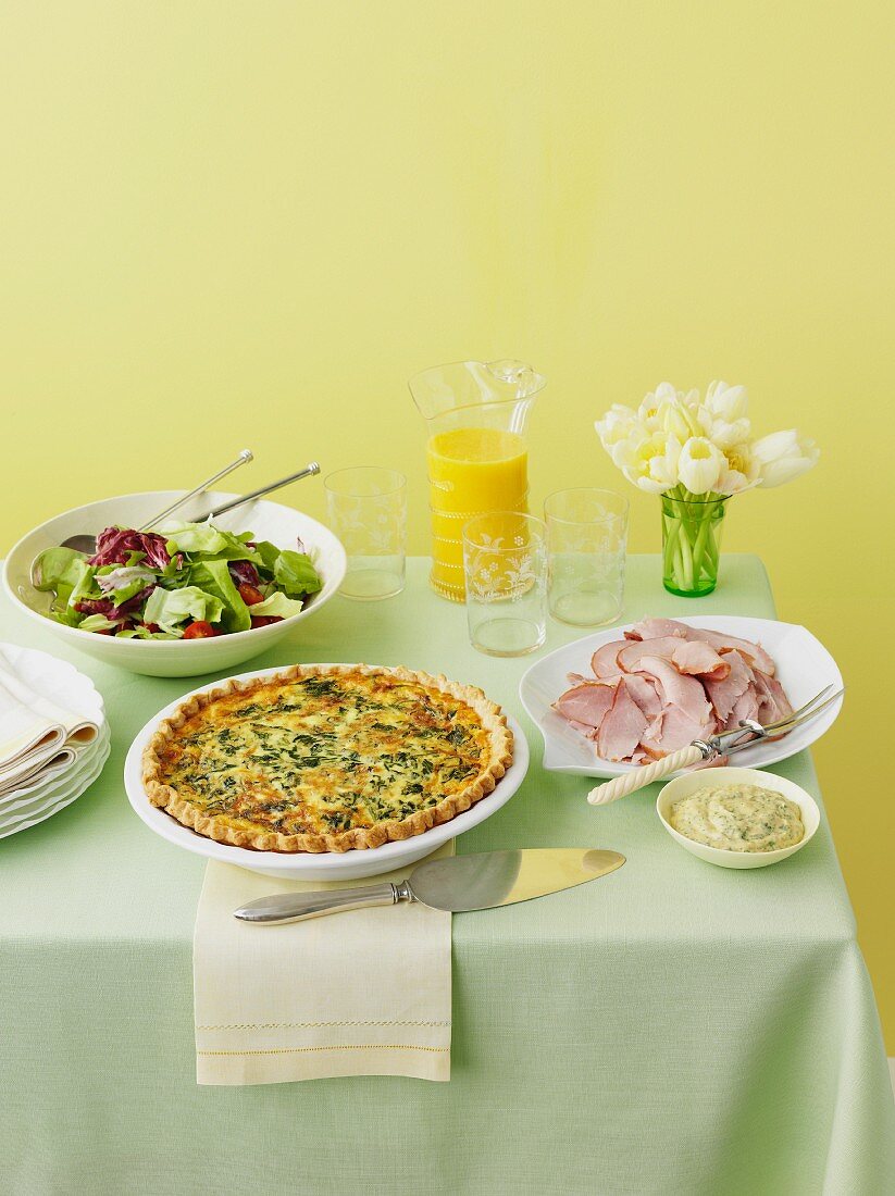 Frühlingshafter Tisch mit Spinatquiche, Schinken und Salat