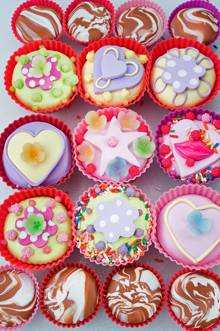 overview o of coloured cup cakes in red and pink plastic cake covers decorated with hearts, lips and sweets
