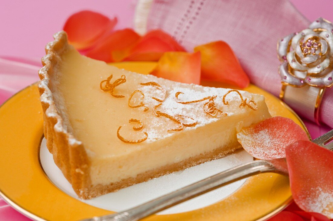 close up of a single serving of lemon pie slice on a yellow and gold ceramic plate with a pink table cloth and napkin with orange rose petal