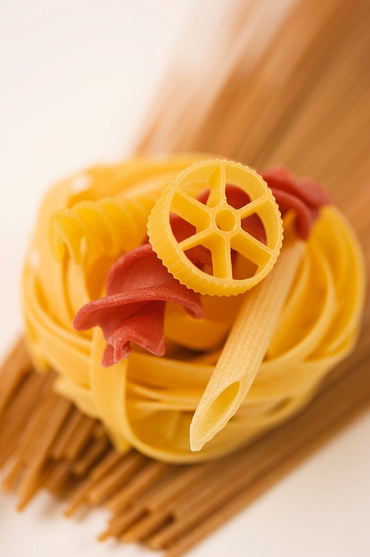 close up of various types of uncooked pasta, rotini, fettucine, spagetti, penne rotelle, rotini and tagliatelle on a white background