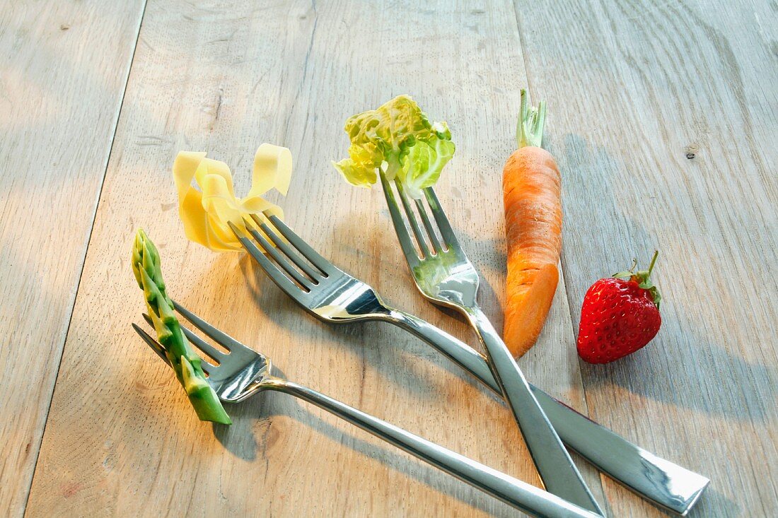 Forks with asparagus, pasta and salad leaves, with a carrot and a strawberry to one side