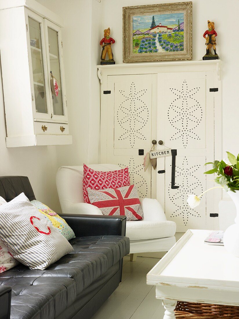 Leather sofa, upholstered chair, coffee table, wall-mounted cabinet and oil painting and figurines on kitchen cupboard in corner of kitchen