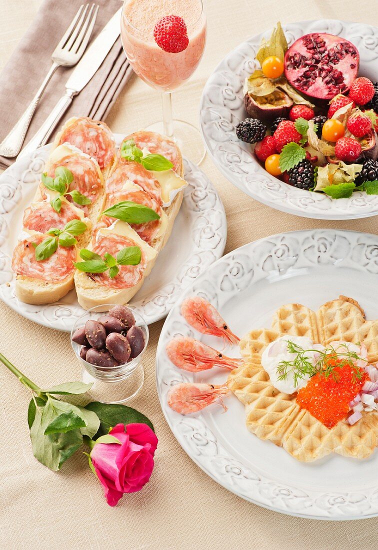 Frühstück mit Kaviar-Waffel, belegten Broten, frischen Früchten und einem Erdbeer-Mango-Smoothie