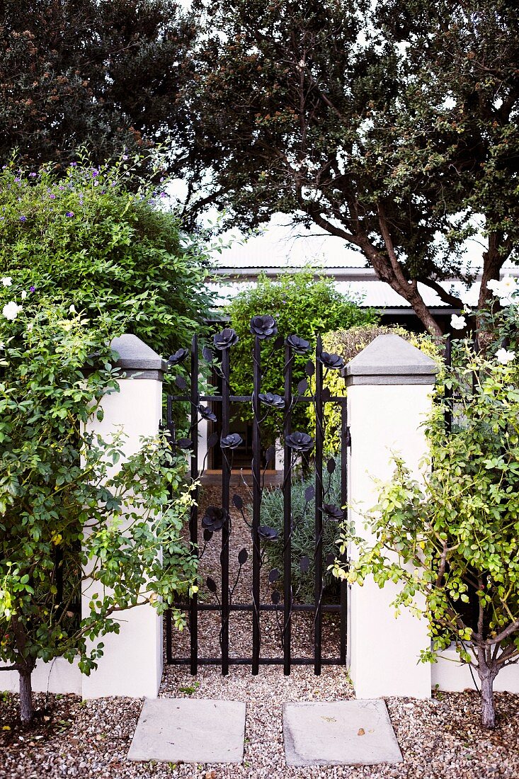 Wrought iron garden gate with floral motif and gravel path leading to house