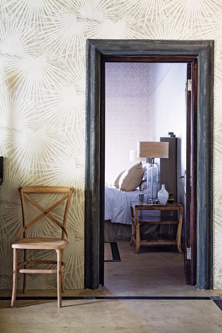 Simple wooden chair against wallpaper with sunburst pattern next to open door leading to bedroom