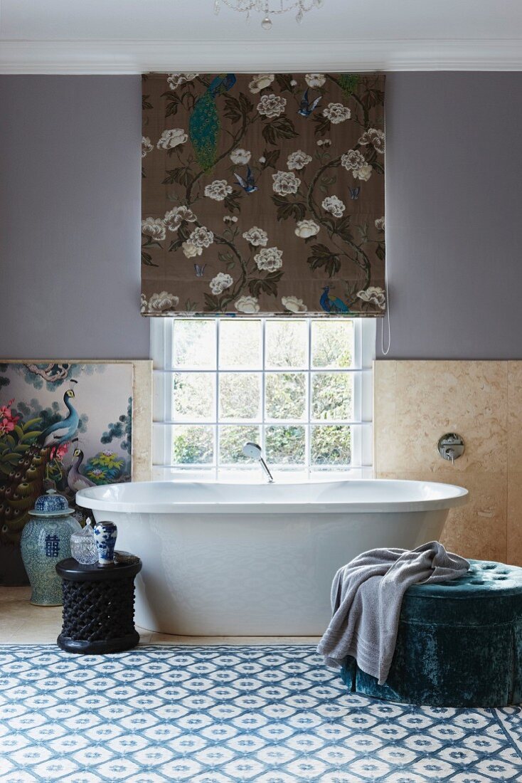 Picture of bird leaning on wall and Chinese porcelain vase next to free-standing bathtub below lattice window in bright bathroom