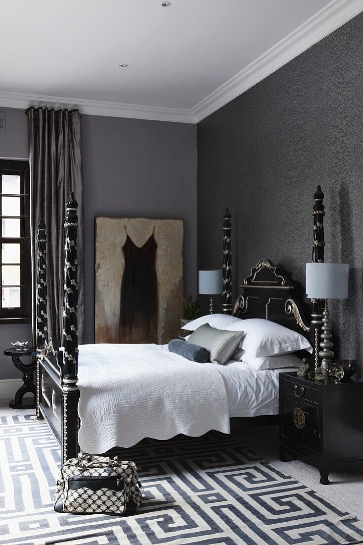 Grey bedroom with artistic, Chinese double bed with tall, silver-ornamented bedposts; rug with woven, geometric pattern on floor