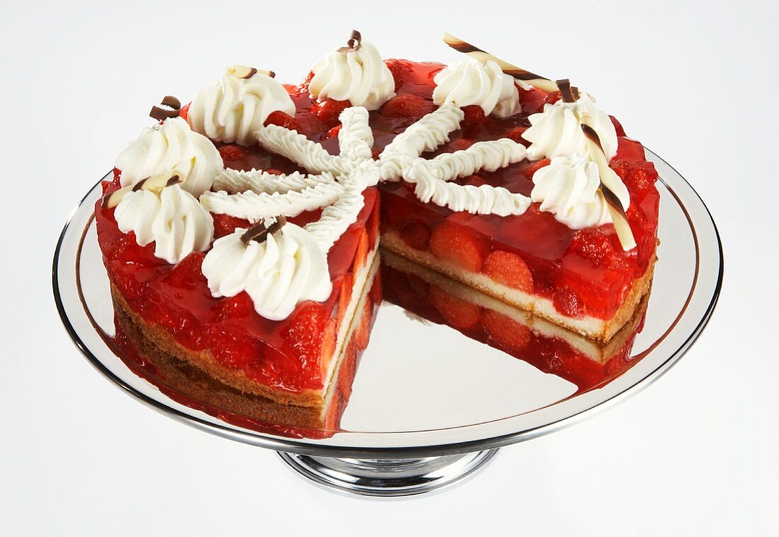 Strawberry layer cake, with a slice removed, on a silver cake stand